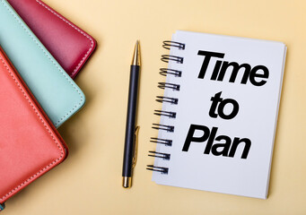 Multi-colored diaries lie on a beige background next to a pen and a notebook with the words TIME TO...