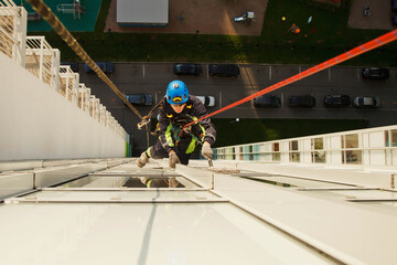 Industrial mountaineering worker hangs over residential building while washing exterior facade glazing. Rope access laborer hangs on wall of house. Concept of urban works. Copy space