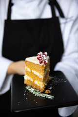A piece of delicious carrot cake on a black tray in the hands of a skilled chef