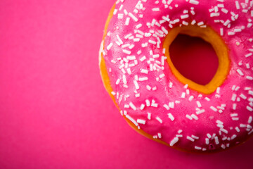 Detailed studio photo of a pink donut with sprinkles on pink background. Selective focus, shallow depth of field.