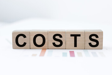 Cost, expense or company profit and loss concept, cube wooden block with alphabet combine word COSTS on the table.