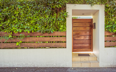 Obraz na płótnie Canvas contemporary house entrance natural wood door and fence with foliage by the sidewalk