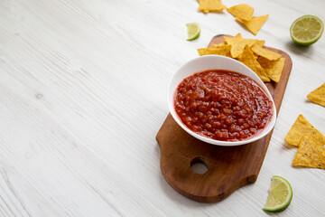 Homemade Tomato Salsa and Nachos on a rustic wooden board on a white wooden table, side view. Copy space.
