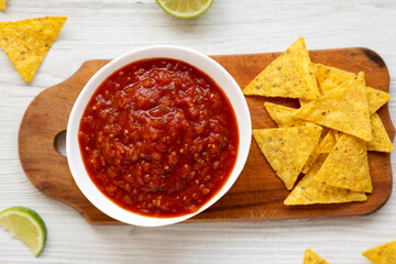 Homemade Tomato Salsa and Nachos on a rustic wooden board on a white wooden background, top view. Flat lay, overhead, from above.