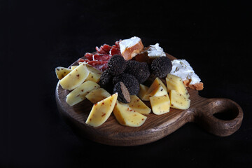 Truffles and cheese on a round wooden Board. Photo on a black background. Top view.