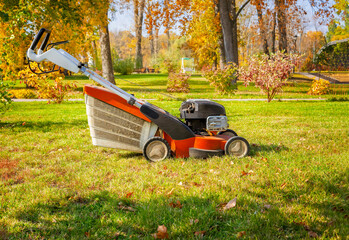 Lawn mower machine on green grass in autumn park.