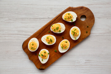 Homemade Deviled Eggs with Chives on a rustic wooden board on a white wooden table, top view. Flat...