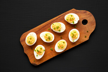 Homemade Deviled Eggs with Chives on a rustic wooden board on a black background, top view. Flat...