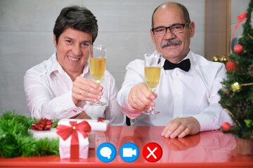 Senior couple celebrating christmas toasting with champagne to the camera on a video call. Christmas celebration concept.
