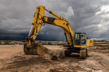 Fototapeta na wymiar Excavator at a construction site surrounded by dramatic clouds