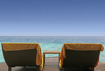 two chairs with towels and table on the wooden bungalow terrace overlooking the ocean