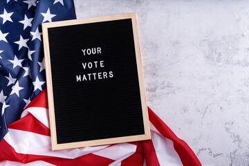 Letterboard sign with the words your vote matters with American flag on white marble background