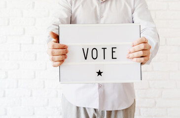 Man holding lightbox with the word Vote on white brick background