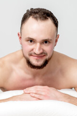 Obraz premium Young caucasian man lying on front on table spa, waiting for beauty treatment and looking at camera