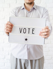 Man holding lightbox with the word Vote on white brick background