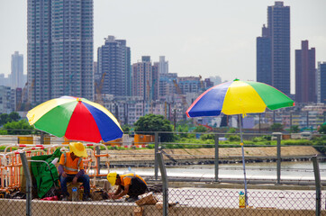 Construction workers work on building site under sun umbrellas in heat during summer in Hong Kong,...