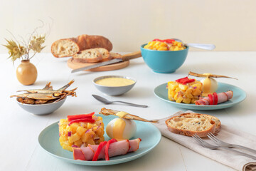 Henri Egg, tasty brunch or snack. Boiled eggs and smoked sprats fish with mayonnaise, ham and potato salad. White wooden table, no people.