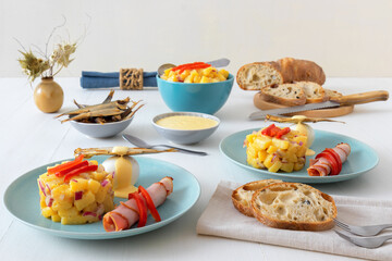 Henri Egg, tasty brunch or snack. Boiled eggs and smoked sprats fish with mayonnaise, ham and potato salad. White wooden table, no people.