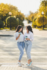 Two people women friends in jeans and shirts are standing near the door drinking coffee and chatting outdoors