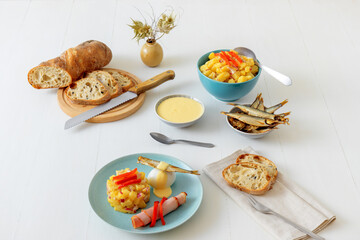 Henri Egg, tasty brunch or snack. Boiled eggs and smoked sprats fish with mayonnaise, ham and potato salad. White wooden table, no people.
