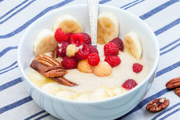 Delicious amaranth with butter, fresh raspberries and banana, pecans and almond chips. Plant-based breakfast. Healthy colorful gluten free concept.
