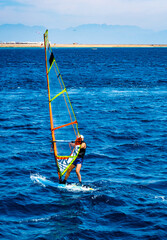 Man spending leisure with extreme windsurfing sport in blue sea with sand beach on background