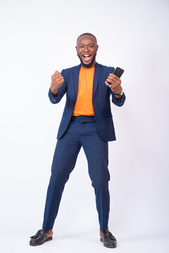 excited african business man celebrating while holding a phone, standing against a white background