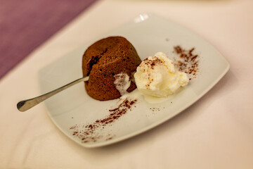 Selective shallow focus of hot chocolate souffle lava cake with cream served with spoon and beautiful stylish white square plate