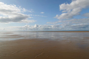 Empty beach at low tide with blue skies and white clouds - UK