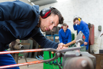 blacksmith holds metal with tongs and hammers on anvil