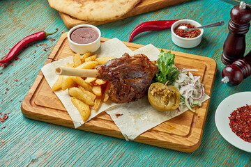 Lamb shank barbecued on the fire with red sauce and potatoes on a green background. Eastern cuisine