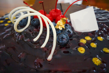 Delicious cake with dark and white chocolate, red cherry and blueberry jam topping on wooden table. Festive cake, restaurant dish.                               