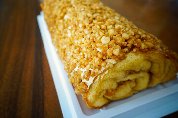 sponge cake roll with caramel nuts topping on wooden table                               