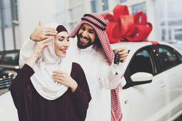 A man smiles and gives a woman keys to a new car.
