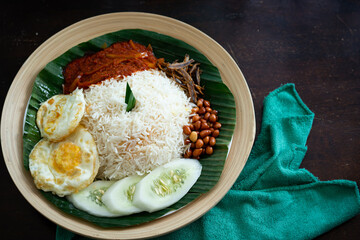 Traditonal Malaysia Asian food Nasi Lemak on a banana leaf in a wooden bamboo plate.