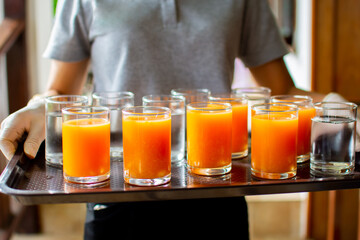 A glass of orange juice and a glass of water on a stool served to the hotel guests