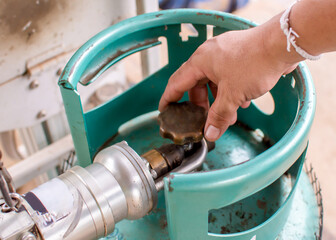 The silver dispenser is connected to the gas cylinder valve and the male operator's hand turns to...