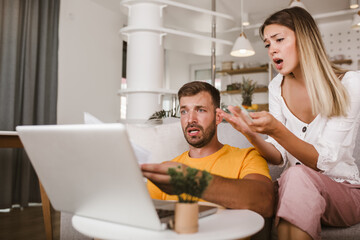 Portrait of young couple paying bills online using laptop and credit card.