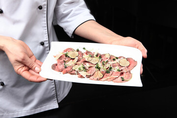 Obraz na płótnie Canvas Roast beef with black truffles. The finished dish is in the hands of the chef. Unrecognizable person. Photo on a black background. Top view.
