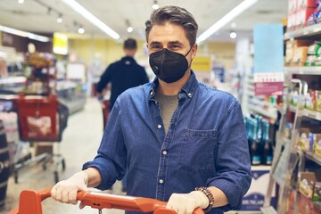 Man buying groceries in supermarket, wearing black medical face mask while shopping in grocery store. Covid-19 virus prevention.