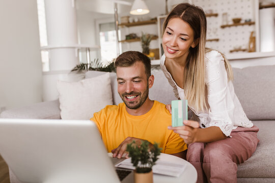 Portrait Of Young Couple Paying Bills Online Using Laptop And Credit Card.