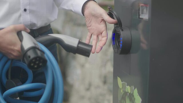 Close up of a modern electric car charger being attached to a silver charging station by a male person wearing a white shirt. Shot in slow motion in 4K.