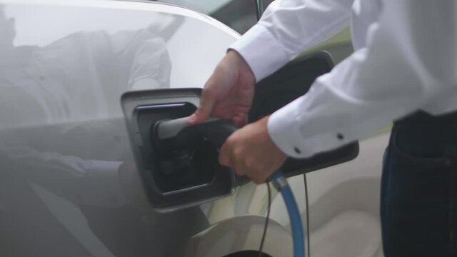 Close up of a modern electric car charger being attached to a silver electric car by a person wearing a white shirt. Shot in slow motion in 4K.