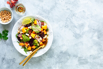 Fresh vegetable salad with beets, arugula, red onions, sorrel, chickpeas, peaches and grapes in a white plate on a white stone background. Top view