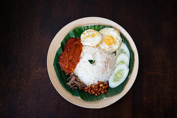 Traditonal Malaysia Asian food Nasi Lemak on a banana leaf in a wooden bamboo plate.
