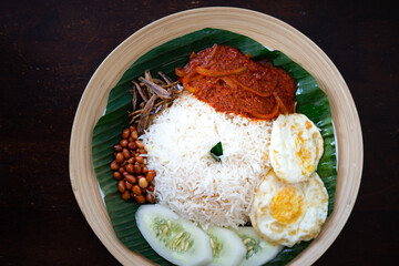 Traditonal Malaysia Asian food Nasi Lemak on a banana leaf in a wooden bamboo plate.