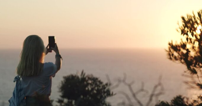 Woman holding phone and makes photo of sunset over the sea horizon. Summer holiday vacation weekend.