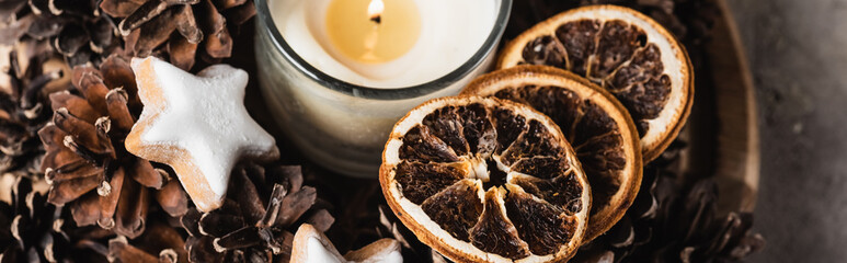 Panoramic shot of scented candle with cookie and pine cones
