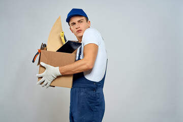 man in working uniform with a box in his hands tools loader delivery light background