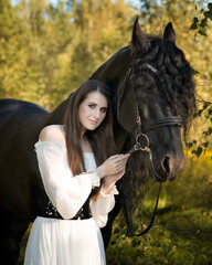 Woman in white dress with big black horse in autumn forest